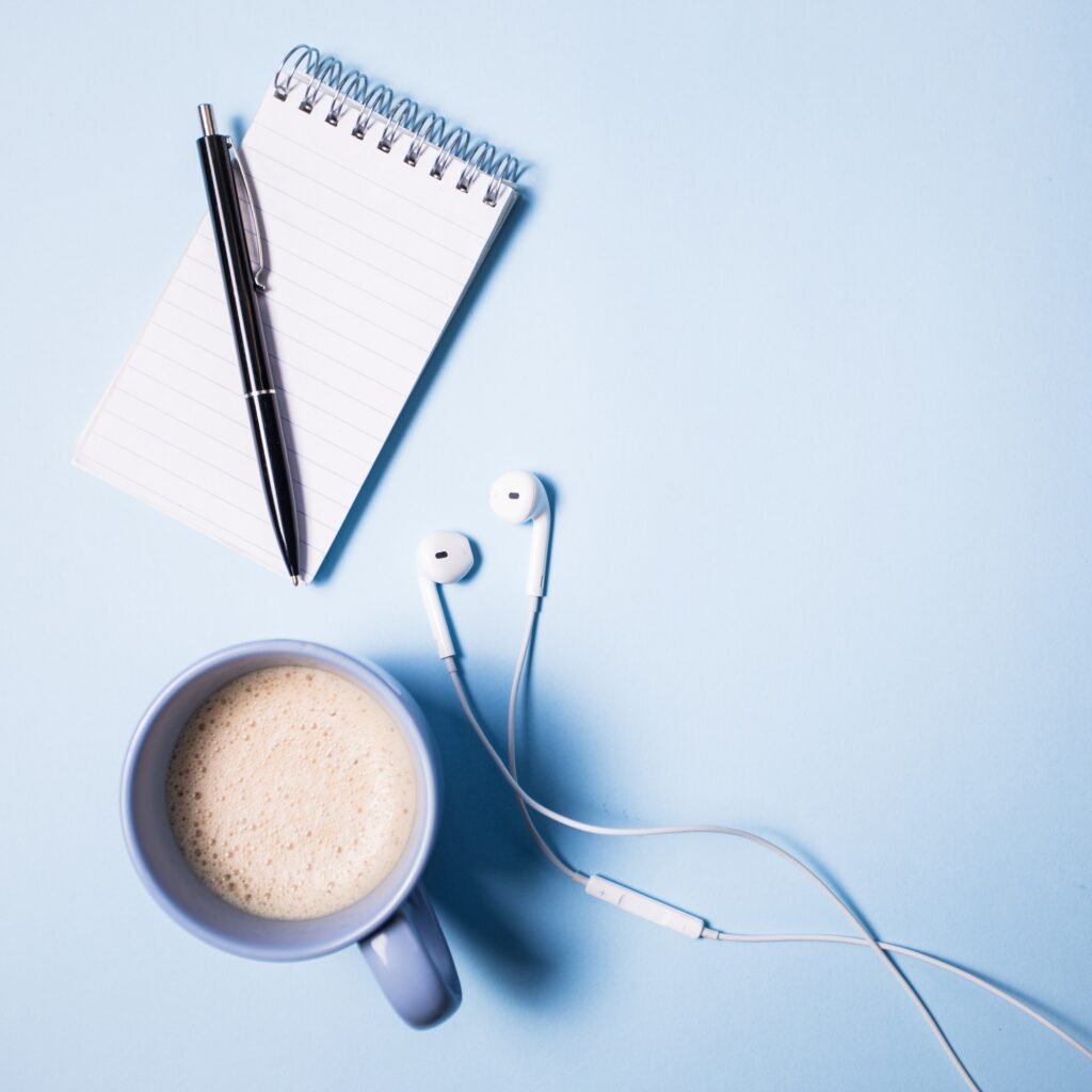 office supplies top view on opened notebook pen headphone laptop and cup of coffee on blue