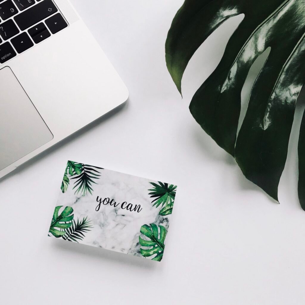 top view laptop on white background desk with postcard monstera texture inspirational quote you can e1669607027334